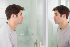 side view of a tensed young man looking at self in mirror in the bathroom