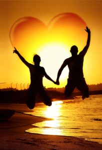 13077536 - happy young couple jumping, holding hands with heart shape in the sky, symbol of happiness, family playing outdoor, sunset on the beach, fun romantic honeymoon vacation, love concept